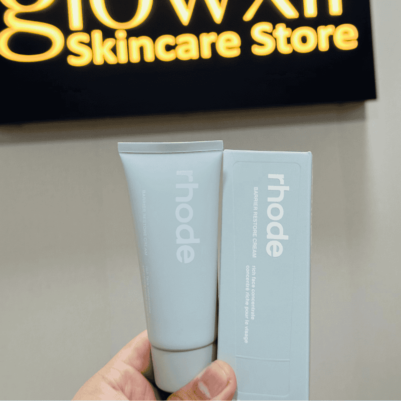 Tube and box of 'rhode' skincare product held in front of a 'Glow Skin Care Store' sign.